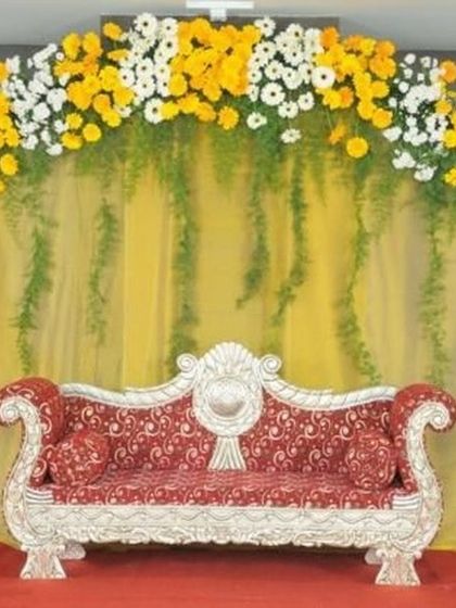 A simple yet elegant stage design featuring a floral arch of yellow and white daisies. This setup is perfect for a day function or a Haldi ceremony, paired with a classic red and silver sofa.