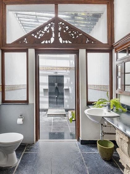 A spacious bathroom with an open-air section, featuring beautiful wooden carvings and traditional tile work.
