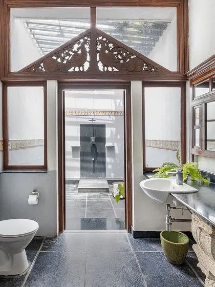 The open-space bathroom in the Arundati suite, featuring a skylight and traditional wood-carved details, blends nature with luxury.