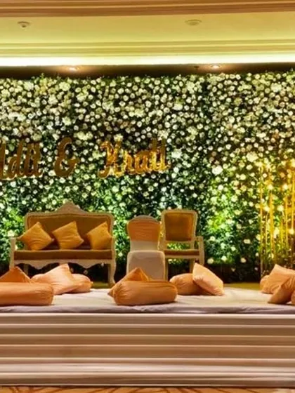 A stunning reception stage featuring a full wall of white and green flowers. The couple's names in gold lettering and the warm floor lighting create a dreamy and romantic ambiance.
