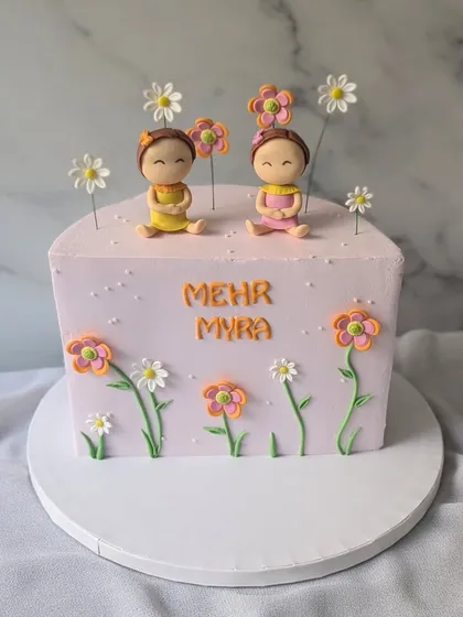 A sweet half-birthday cake for twin girls, Mehr and Myra. This square cake is decorated with two cute figurines sitting in a field of flowers.