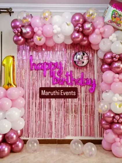 A pretty pink and white first birthday setup. The balloon arch is accented with butterfly details and a "happy birthday" foil balloon script.