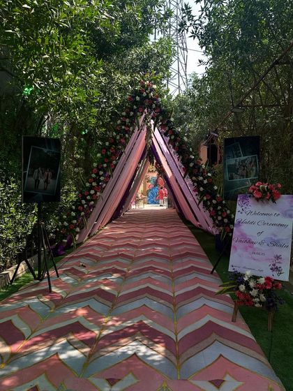 A beautiful tented walkway for a Haldi ceremony, with a pink and white chevron floor runner, floral arch, and personalized welcome sign.