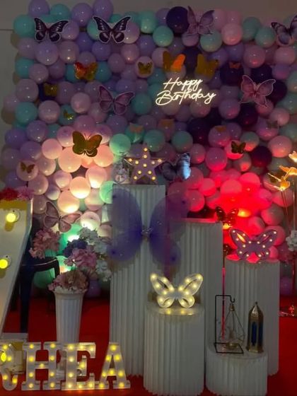A butterfly garden theme against a full balloon wall. This immersive decoration uses pastel balloons, various butterfly cutouts, a 'Happy Birthday' neon sign, and light-up letters and numbers.