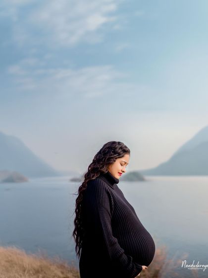 Another angle of the serene lakeside shoot, this photo captures the mother-to-be looking down at her bump with love.