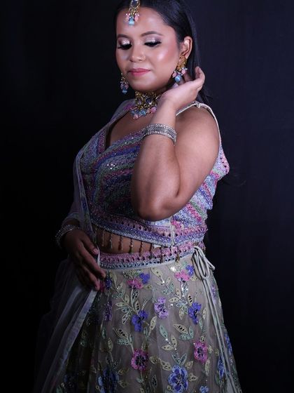 A side view of the happy client in her pastel engagement lehenga, showing the detail on the blouse and skirt against a dark background.