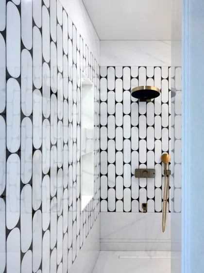 A closer look at the walk-in shower, where the graphic black and white inlay pattern continues. The clean lines of the built-in shelving and the minimalist brass fixtures complement the bold tilework, creating a balanced and modern aesthetic.