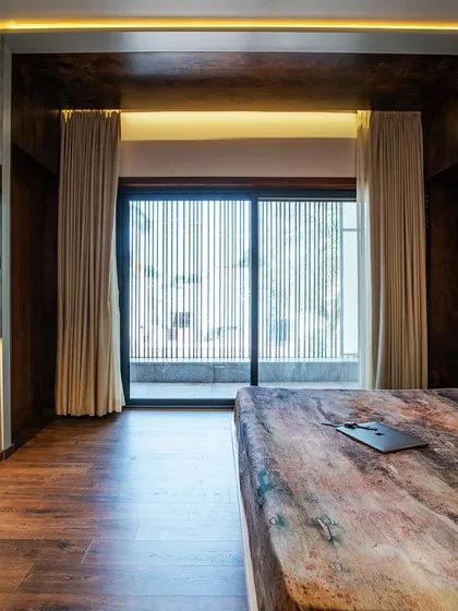 The master bedroom of the "Vertical Nest" project, featuring a floating bed and a unique headboard design combining green leather and concrete-textured panels.