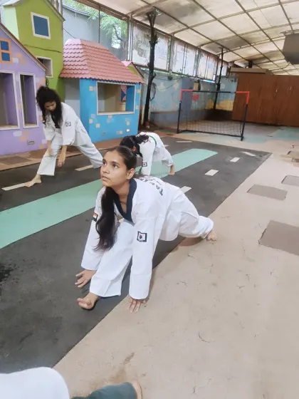 A student holds a lunge stretch, focusing on opening up her hips. This type of dynamic stretching is crucial for kicks like the roundhouse and side kick.