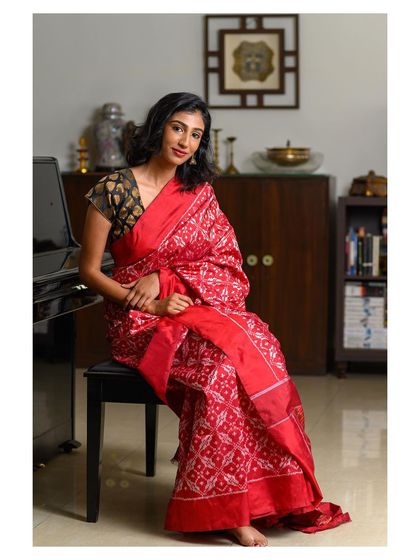 A woman seated gracefully in a stunning red saree. This indoor portrait uses the environment, including the piano, to add a touch of sophistication.