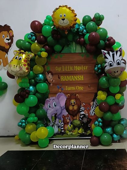 A simple and cute jungle theme backdrop for a first birthday. This design features a round wooden-look flex, a lush green balloon garland, and foil animal heads like a lion, giraffe, and zebra.