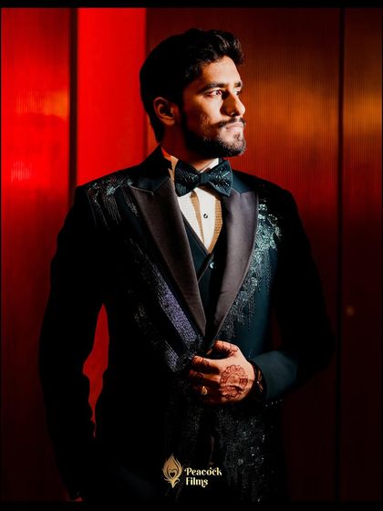 A dapper groom portrait from the Sangeet night. The dramatic red lighting and his sharp tuxedo create a look of pure sophistication and style.