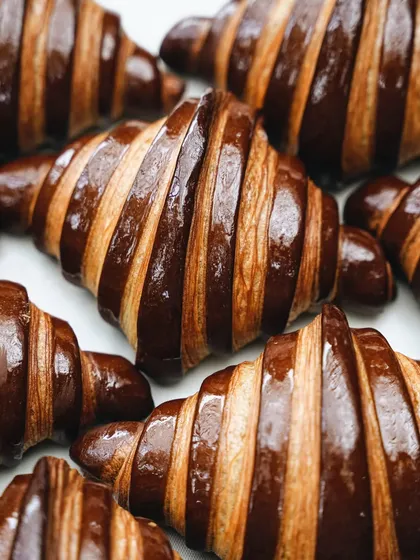 A satisfying top-down shot of perfectly laminated chocolate croissants. The repeating pattern and the contrast between the golden pastry and dark chocolate make for a visually striking image.