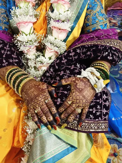 A beautiful shot of a Marathi bride's hands, showcasing the rich, dark stain of her bridal mehendi. The color contrasts beautifully with her traditional green bangles and wedding attire.
