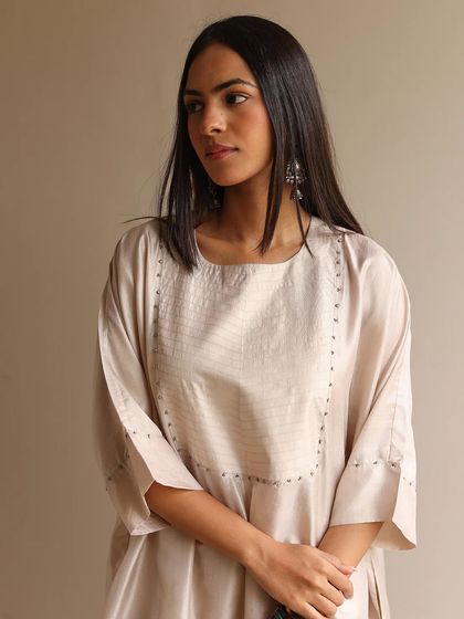 A model showcasing a sophisticated beige kurta with a simple, elegant cut and subtle stitch detailing around the neckline.