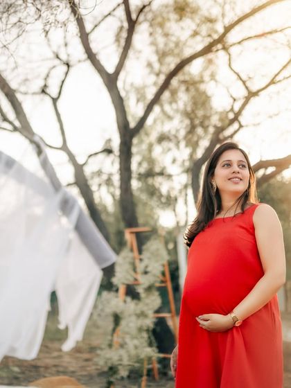A radiant mom-to-be in a vibrant red dress, enjoying the golden hour light outdoors. Her happy expression and the warm sunlight create a joyful and hopeful maternity portrait.