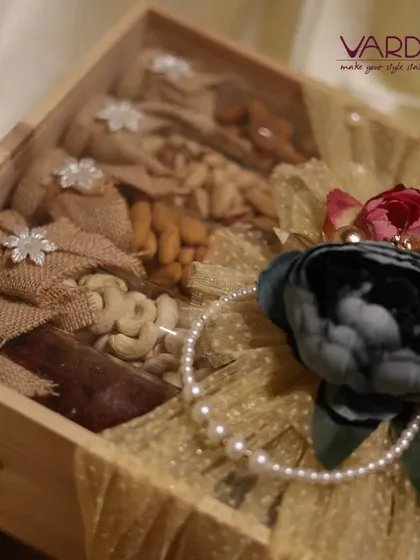This rustic yet elegant wooden gift box is filled with an assortment of premium nuts like cashews and almonds, packaged in charming burlap pouches. The box is adorned with a decorative floral and pearl arrangement.