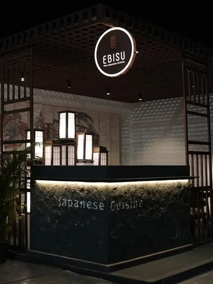A wide shot of the 'Ebisu' Japanese fine-dining pop-up we created for the India Art Fair. The design features a structured, dark wood frame, a glowing circular brand sign, and traditional Japanese lanterns to create an authentic and inviting atmosphere at night.