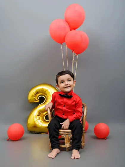 A joyful portrait of a two-year-old boy sitting with red balloons for his birthday celebration.