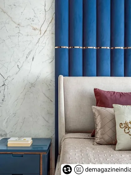 The master bedroom in 'Fifty Two' features a tall, upholstered blue headboard with gold accents, set against a white marble wall.