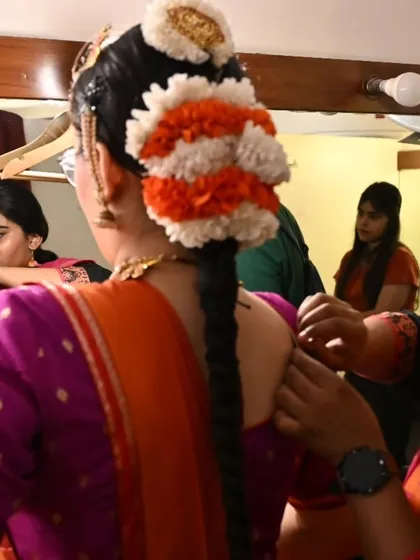 The intricate process of getting ready for a performance. A student helps another with her hair and costume, a common sight in the bustling energy of the green room.