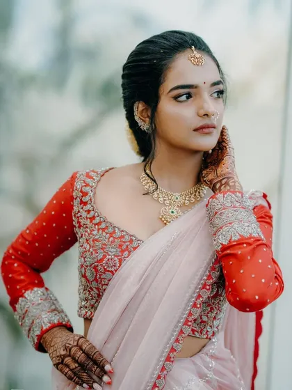 A striking bridal portrait. The custom red blouse with full-sleeve silver embroidery creates a bold and modern contrast with the delicate pink half-saree.