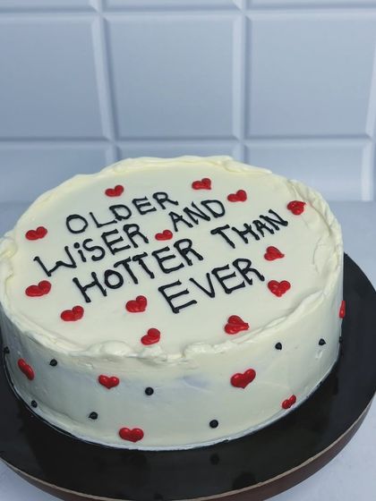 A still shot of the "Older, Wiser, and Hotter Than Ever" cake. The simple design with little red hearts makes the message stand out. It's a celebration of aging gracefully and confidently.