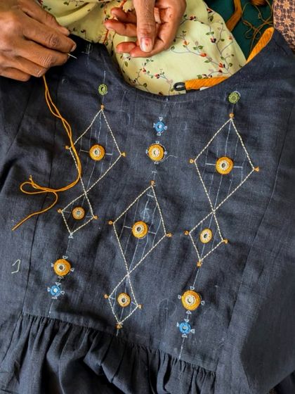 The making of our Paheli collection. Here, an artisan carefully embroiders a geometric pattern with mirror work onto a dark cotton fabric, bringing the design to life one stitch at a time.