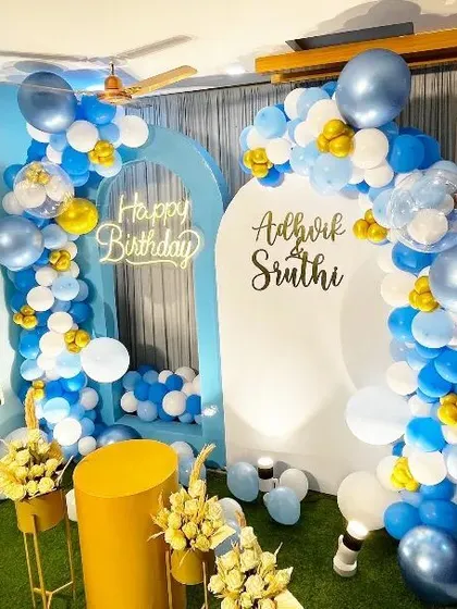 A closer view of the blue and white double-arch setup, highlighting the balloon arrangement and floral stands.