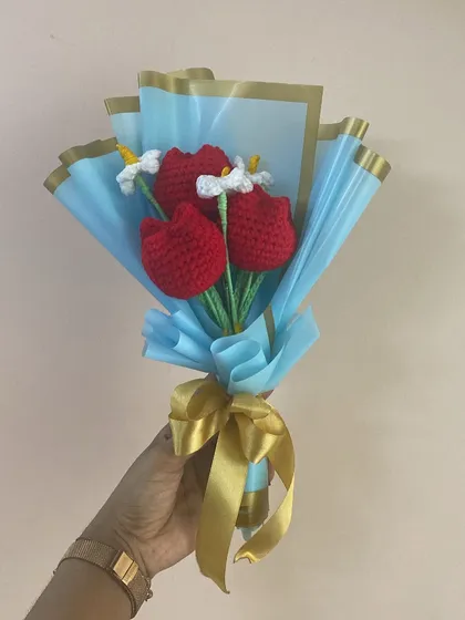 The red tulip and daisy bouquet held up, showing the elegant blue and gold wrapping.