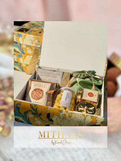 An open view of a custom hamper in a beautiful floral-patterned box. Inside, a mix of my signature treats like boondi, chocolate bars, and other jarred sweets are elegantly arranged.