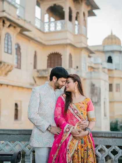 An intimate embrace between the couple, with their colorful traditional outfits popping against the neutral tones of the palace facade.