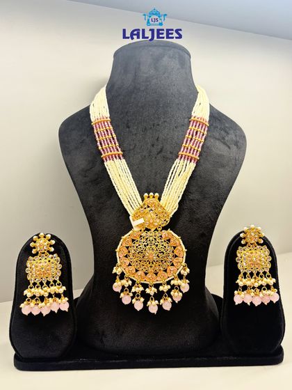 A stunning golden rani haar with a large circular pendant and delicate pink bead drops, perfect for a soft, royal look.