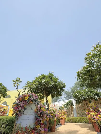 The entrance to the vibrant Haldi lunch, with a floral-wreathed welcome sign. The path was lined with terracotta pots filled with colorful flowers, creating a cheerful and inviting entryway.