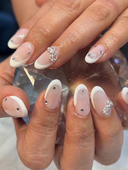 A truly bow-tiful set of nails. This elegant design elevates the French manicure with delicate silver bows and scattered rhinestones for a touch of sparkle.