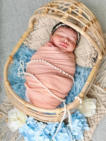 A closer view of the sleeping baby in the cane bassinet, highlighting the delicate features and the textures of the swaddle and props.