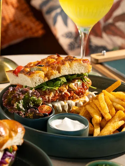 A hearty focaccia sandwich with a side of fries and salad. This is a complete meal shot, perfect for a lunch menu.