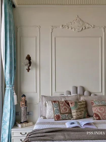Another view of the classic bedroom, showing the ornate wall moldings and a vintage-style sconce. The mix of patterned and solid cushions adds visual interest to the bed.