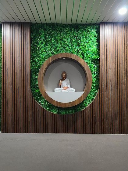 This tranquil meditation wall, featuring a Buddha statue in a circular niche, combines natural elements like a vertical garden with the warmth of wood, creating a perfect spot for finding inner peace.