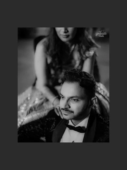 A classic, moody black and white portrait of the groom, with the bride softly in the background. The focus and lighting create a sense of drama and sophistication.