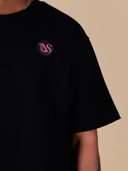 A macro shot of the 'TNS' chest logo on the 'World of Lovers' tee, showing the clean embroidery and quality of the fabric.