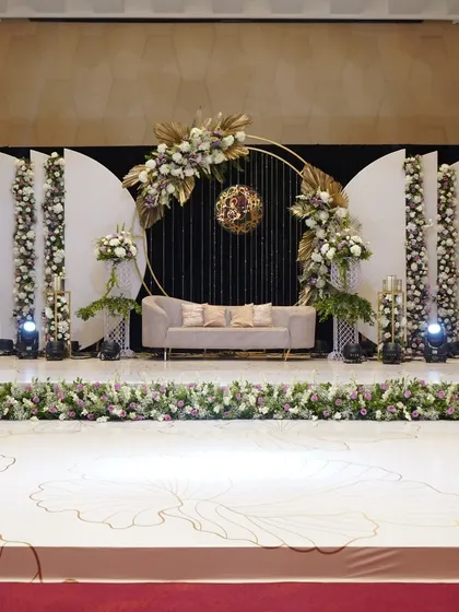 A modern and chic reception stage, featuring a circular backdrop with the couple's monogram, surrounded by beautiful floral arrangements in a soft, muted color palette.