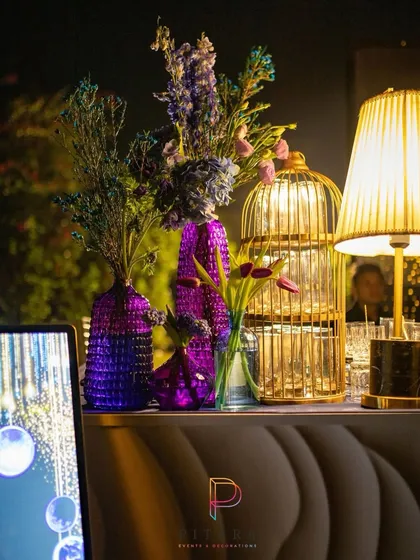 A detail from the bar area, where a golden birdcage, a modern lamp, and textured purple vases holding tulips and dried florals created a stylish, eclectic vignette.