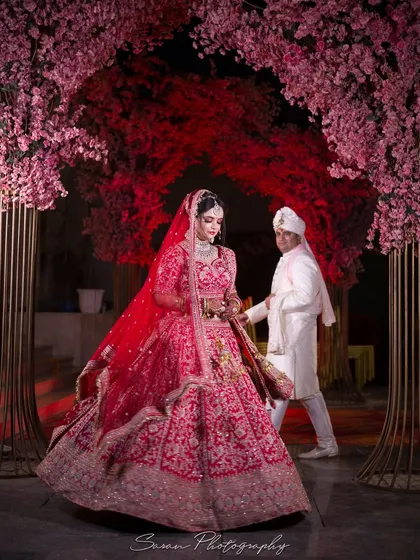 The groom leads his bride for a walk under a stunning pink floral archway, creating a magical wedding portrait.