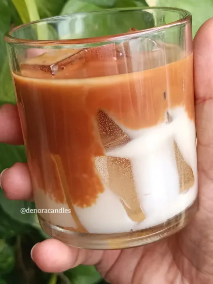 A hand-held view of the iced coffee candle, highlighting the rich brown and white layers.