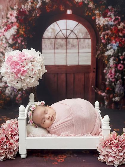 Sleeping in a secret garden. This newborn girl is peacefully napping in a tiny bed, set against a magical backdrop of a floral archway.
