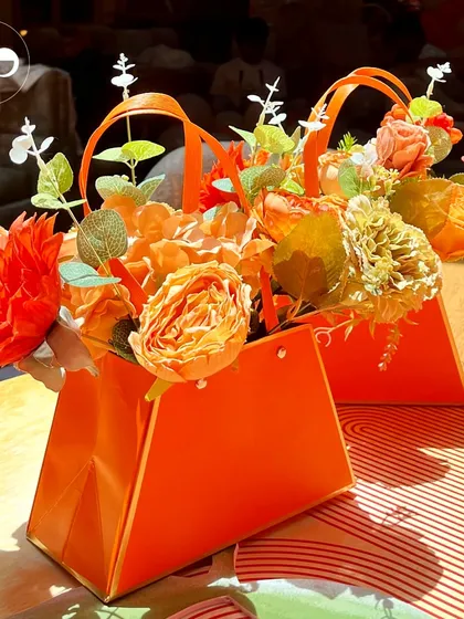 A unique and stylish centerpiece idea. These vibrant orange paper bags hold beautiful arrangements of orange and peach hued flowers, adding a modern and creative touch to the tables at this citrus themed shower.
