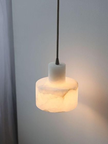 A simple, cylindrical pendant light made from solid marble. The soft glow through the stone creates a warm and calming ambiance.
