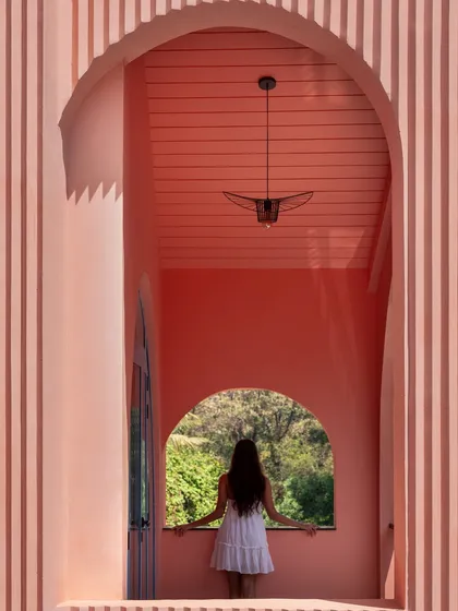 Within the fluted, peach-colored walls of Baia Villas, an arched window frames the lush greenery outside. This composition of form, color, and nature is a quiet moment that captures the project's essence.