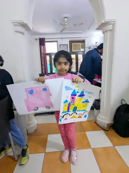 Our little artists are on the move with their vehicle-themed art. Here a student proudly displays her drawings of a pink bus and a magical castle.